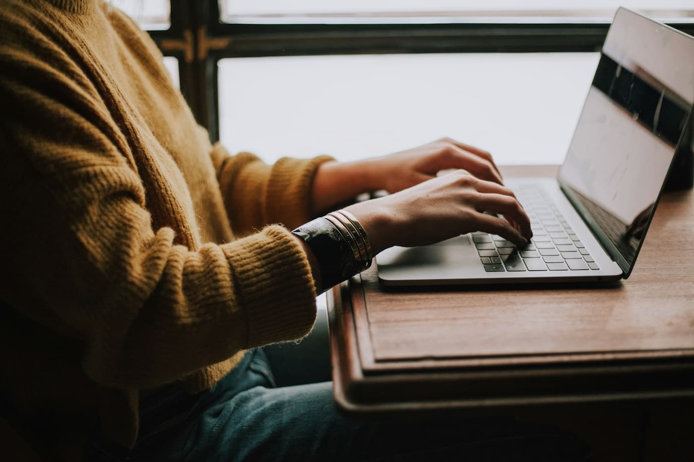 Hands typing on a laptop at a warm, informal workspace
