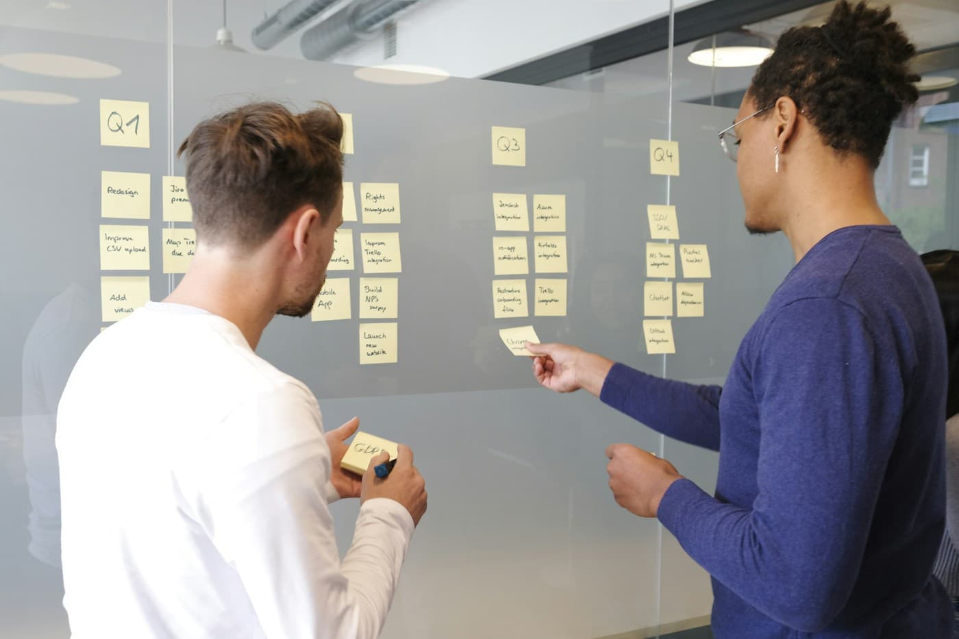 Two product planners arranging notes on a glass roadmap board